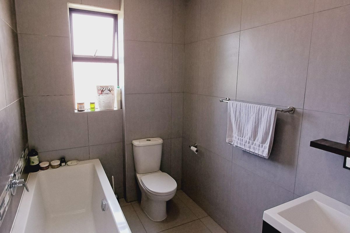 A modern, well-maintained bathroom featuring neutral floor-to-ceiling tiling, a bathtub, a toilet, and a vanity unit.