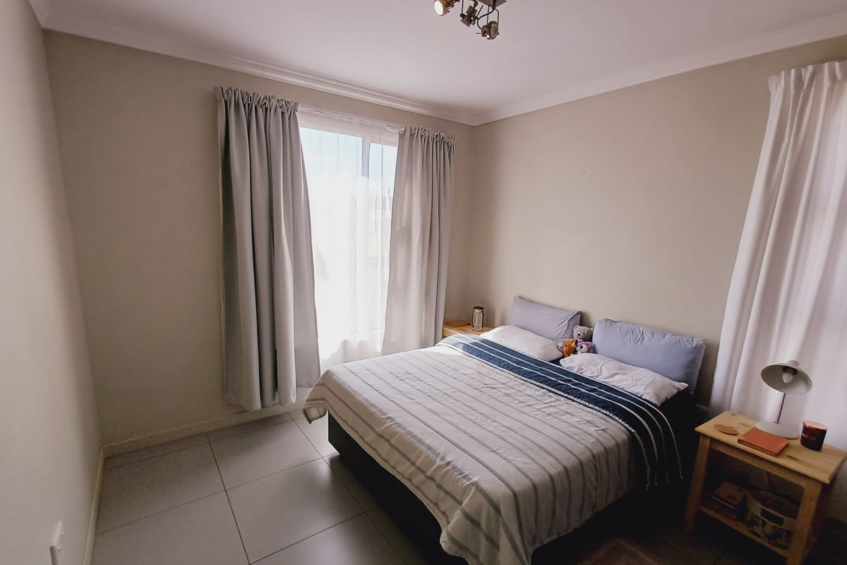 A well-maintained bedroom featuring neutral wall tones, tiled flooring, and a modern ceiling-mounted spotlight fixture, providing a clean and functional living space.
