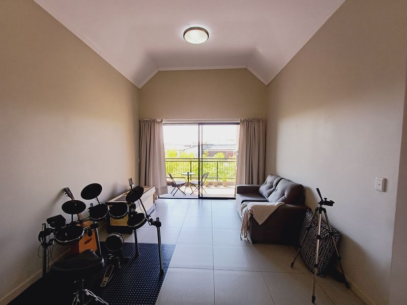 Spacious living room featuring high vaulted ceilings, neutral tiled flooring, and large sliding glass doors leading to a private balcony.