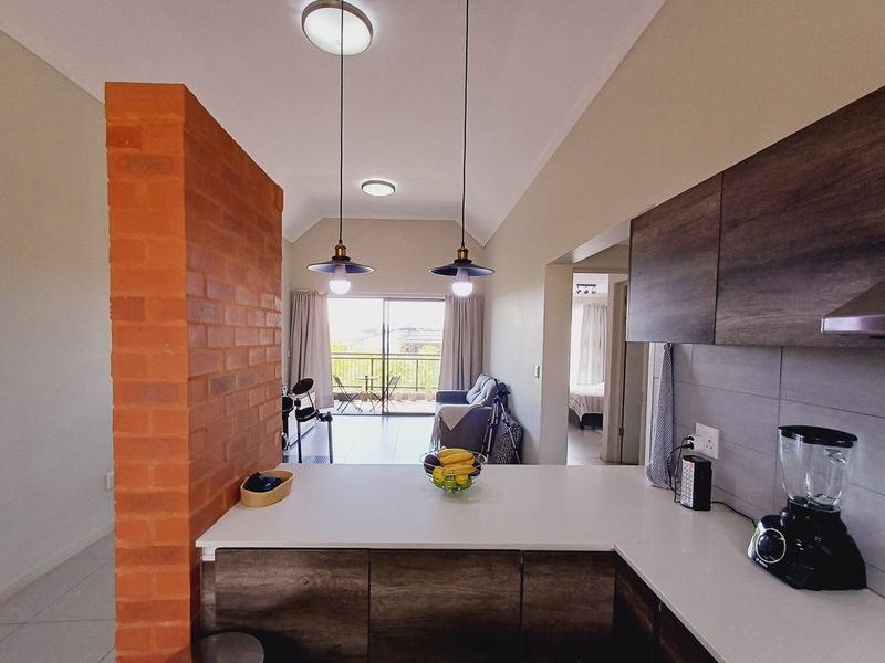 Modern open-plan kitchen and living area featuring an exposed brick wall, sleek cabinetry, stone countertops, and direct access to a balcony.