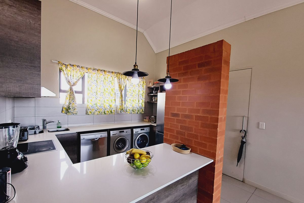 Modern kitchen featuring stone countertops, integrated appliances, and a distinctive exposed brick feature wall, complemented by stylish pendant lighting and tiled flooring.