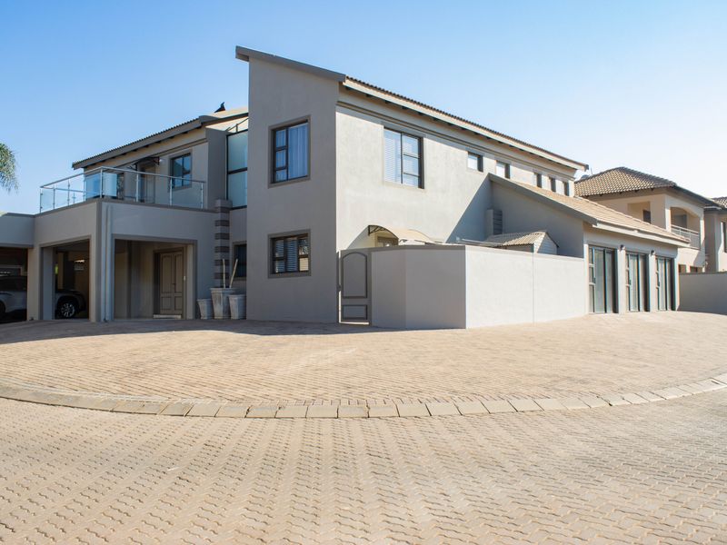 Modern double-story residential property featuring a paved driveway, integrated carport, and an upper-level balcony with glass balustrades.