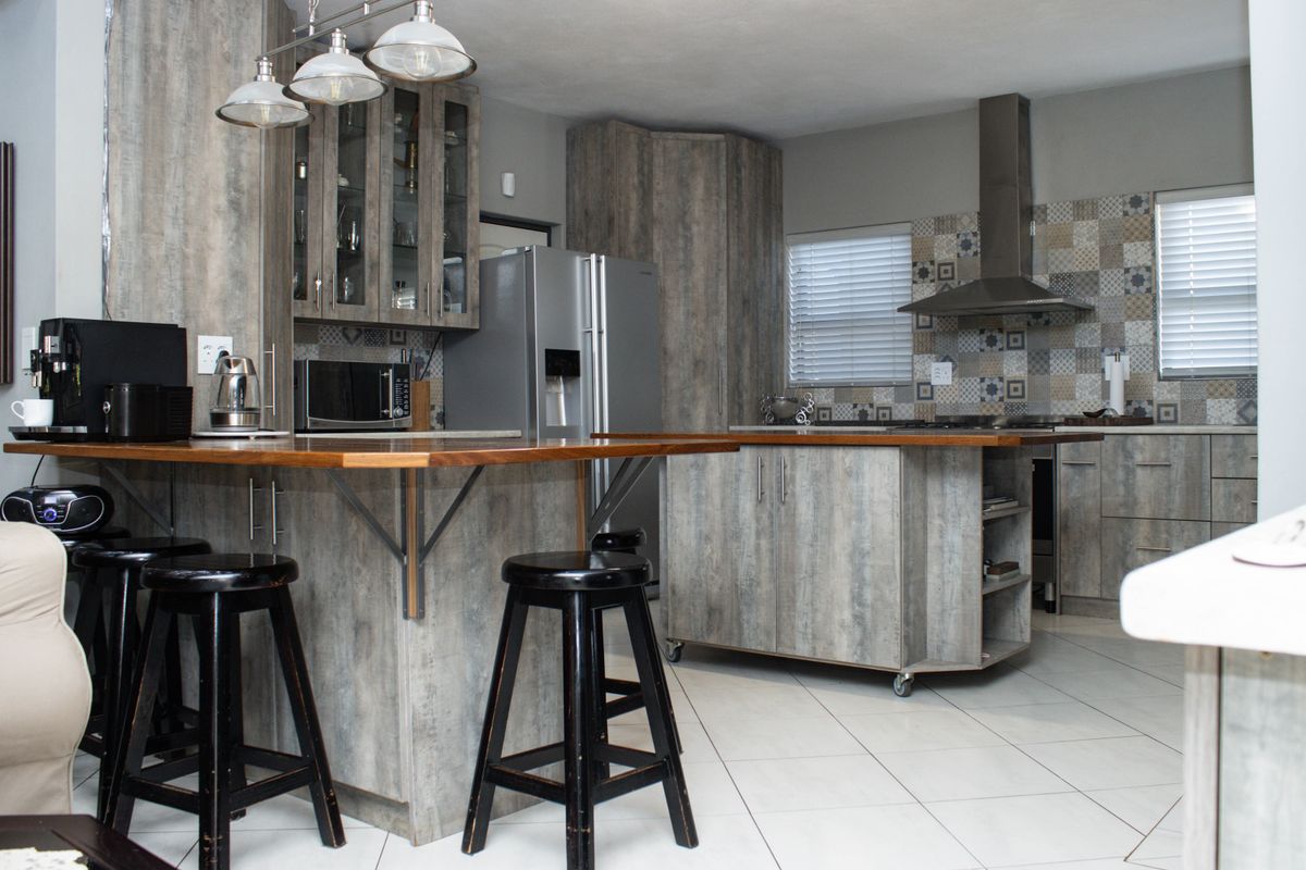 Modern kitchen featuring wood-look veneer cabinetry, a central island with breakfast bar, tiled backsplash, and stainless steel extractor fan.