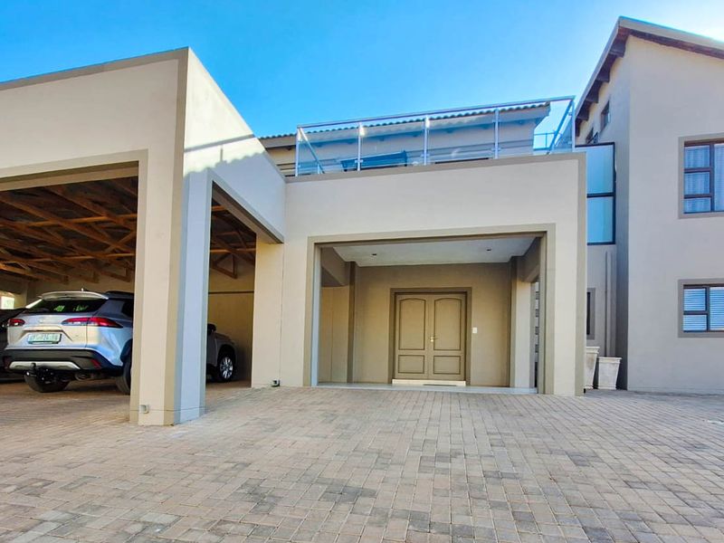 Modern double-storey house exterior featuring a paved driveway, covered double garage, and an upper-level balcony with a glass balustrade.