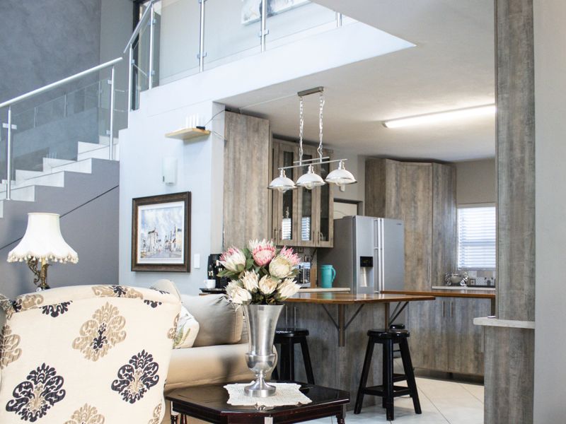 Open-plan living area featuring a modern kitchen with wood-look cabinetry, a breakfast island, and a staircase with a contemporary glass balustrade.
