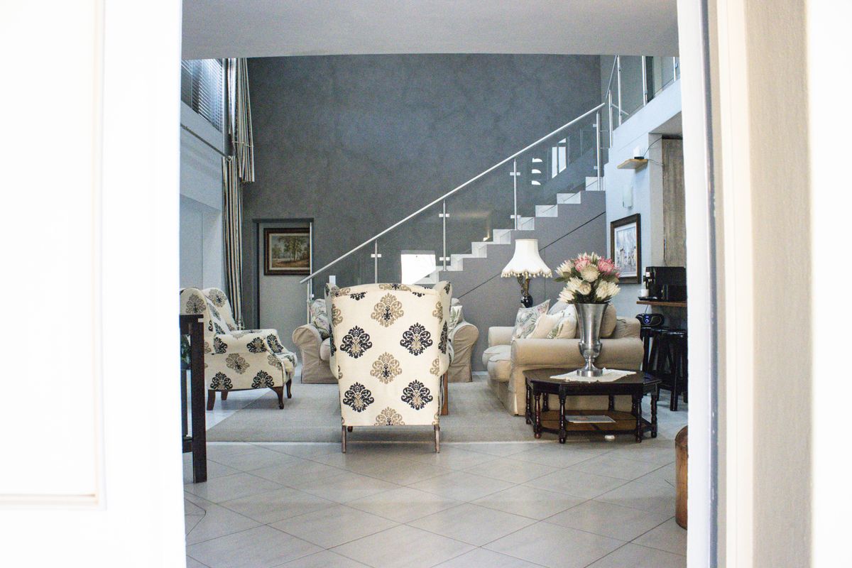 Spacious living area featuring a modern staircase with glass balustrade, double volume ceilings, and neutral tiled flooring.