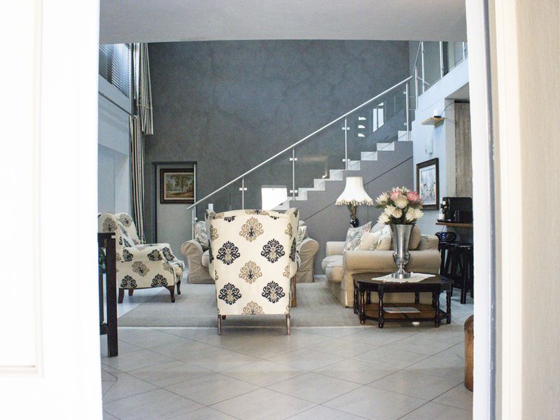 Spacious living area featuring a modern staircase with glass balustrade, double volume ceilings, and neutral tiled flooring.