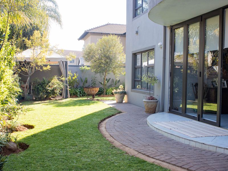 A well-maintained rear garden featuring a curved paved walkway, manicured lawn, and large sliding glass doors providing access to the home.