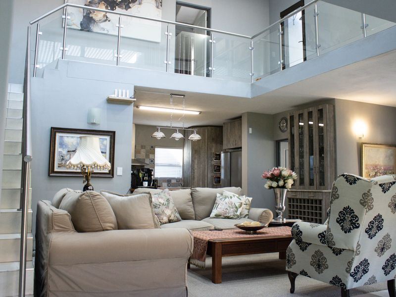 Spacious open-plan living area featuring a double-volume ceiling, modern glass balustrade staircase, and integrated cabinetry with a built-in wine rack.