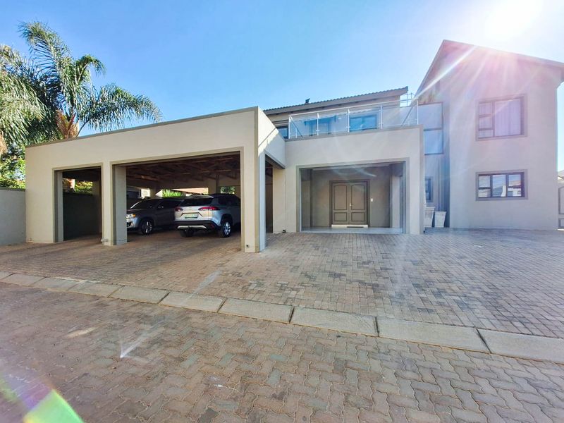 Modern double-story residence featuring a spacious paved driveway, integrated double garage, and an upper-level balcony with glass balustrades.