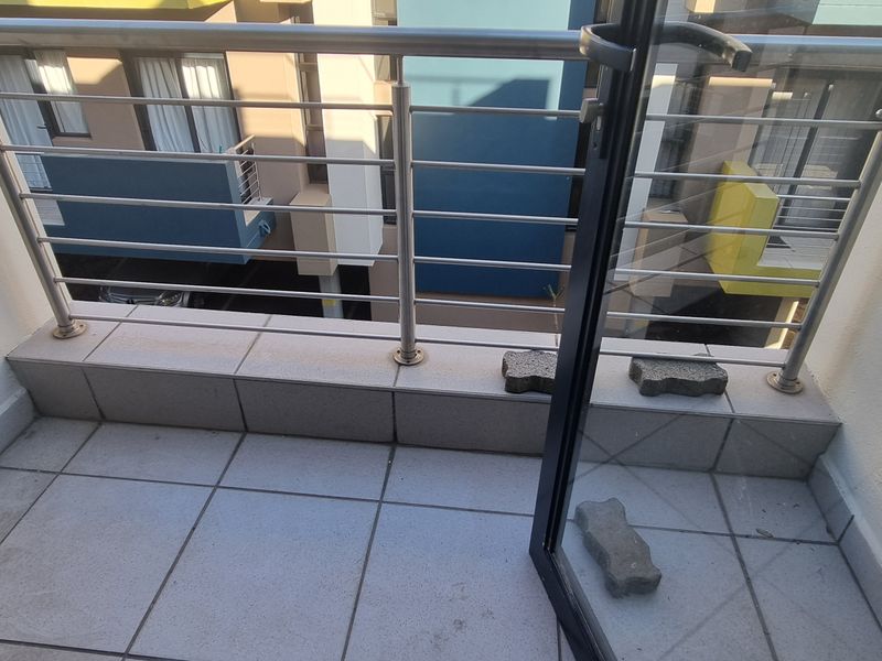 A compact balcony featuring tiled flooring and a modern stainless steel balustrade, accessible via a sliding glass door.