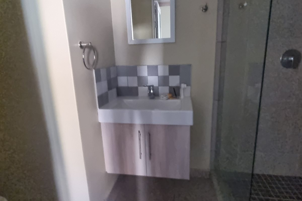 A functional bathroom featuring a modern vanity cabinet with basin, tiled splashback, and a glass-enclosed shower area.