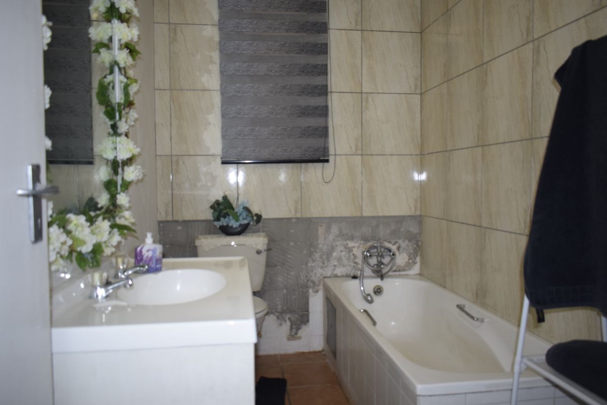 A bathroom featuring a bathtub, vanity basin, and toilet, currently requiring wall repairs and tiling to complete the finishes.