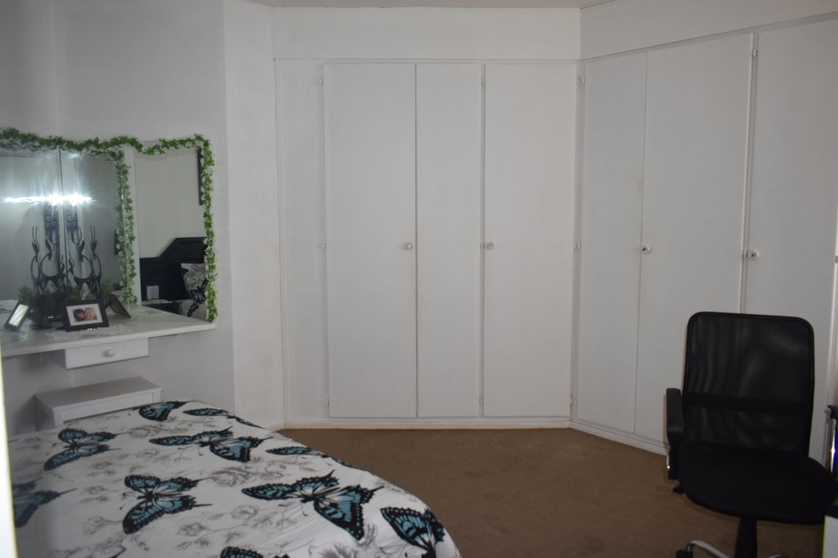 A bedroom featuring extensive white built-in cupboards and a matching built-in vanity unit with mirror.