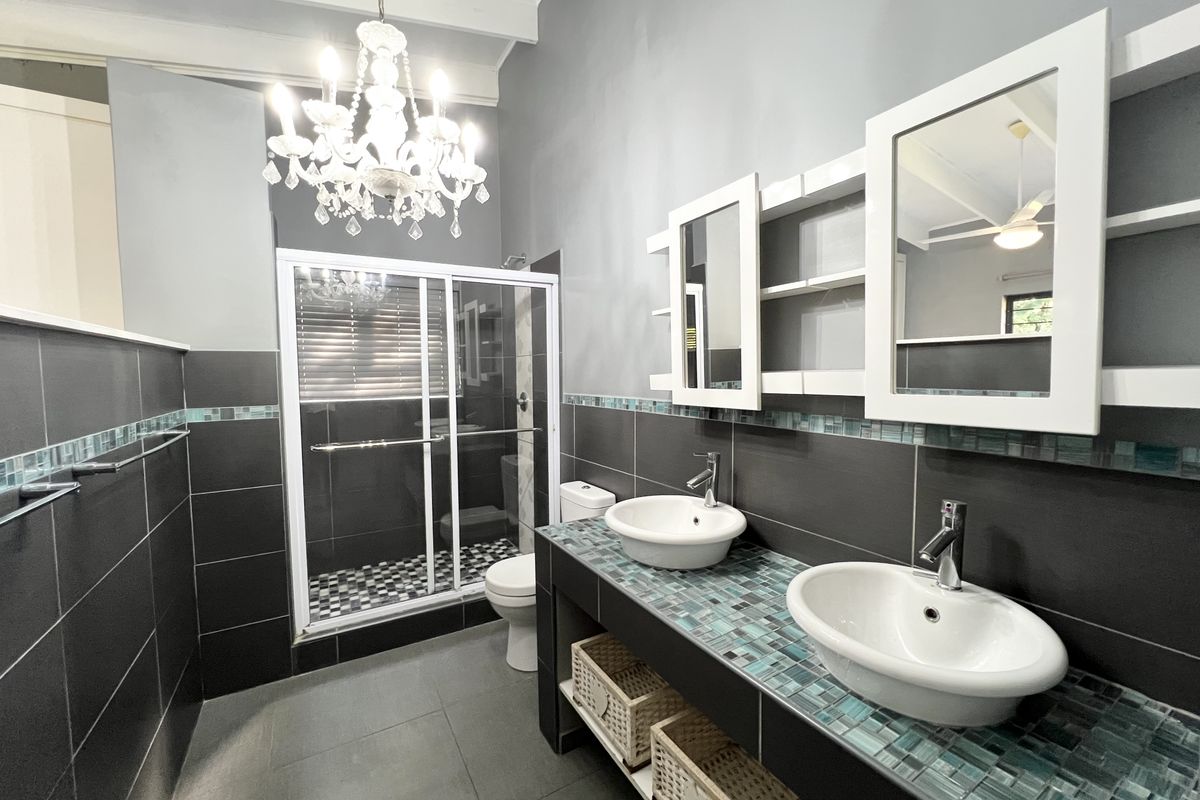 Modern bathroom featuring a double vanity with vessel sinks, mosaic tile backsplash, glass-enclosed shower, and elegant chandelier lighting.