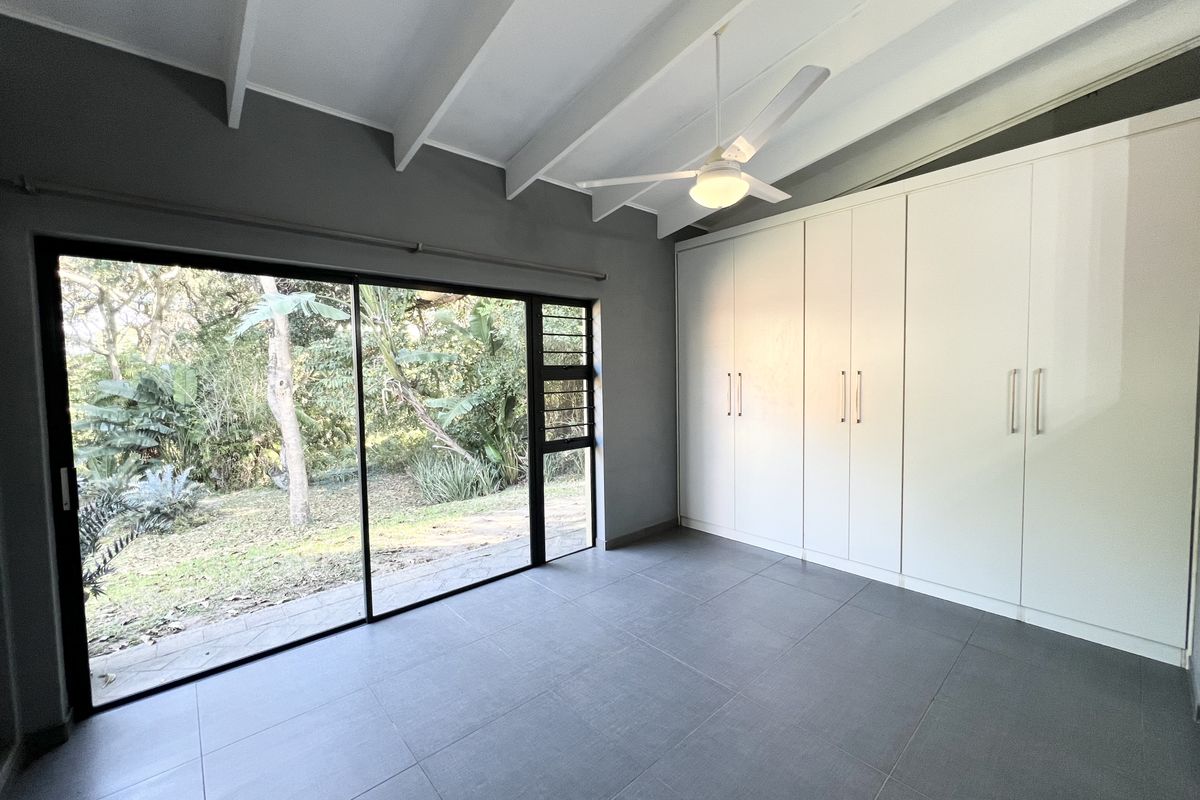 A bright bedroom featuring large sliding glass doors, built-in white cabinetry, tiled flooring, and a vaulted ceiling with a fitted overhead fan.
