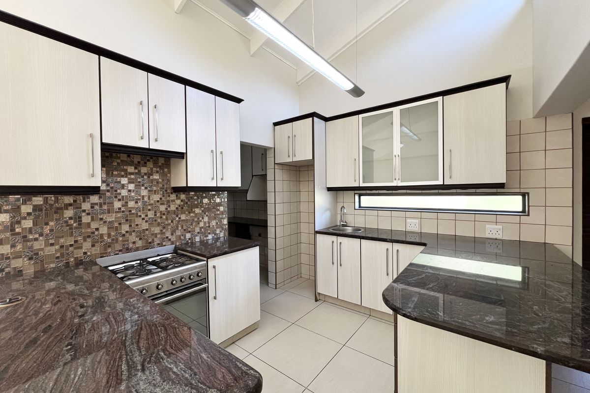 Modern kitchen featuring granite countertops, light wood-grain cabinetry, a gas stove, mosaic tile backsplash, and high vaulted ceilings with integrated lighting.