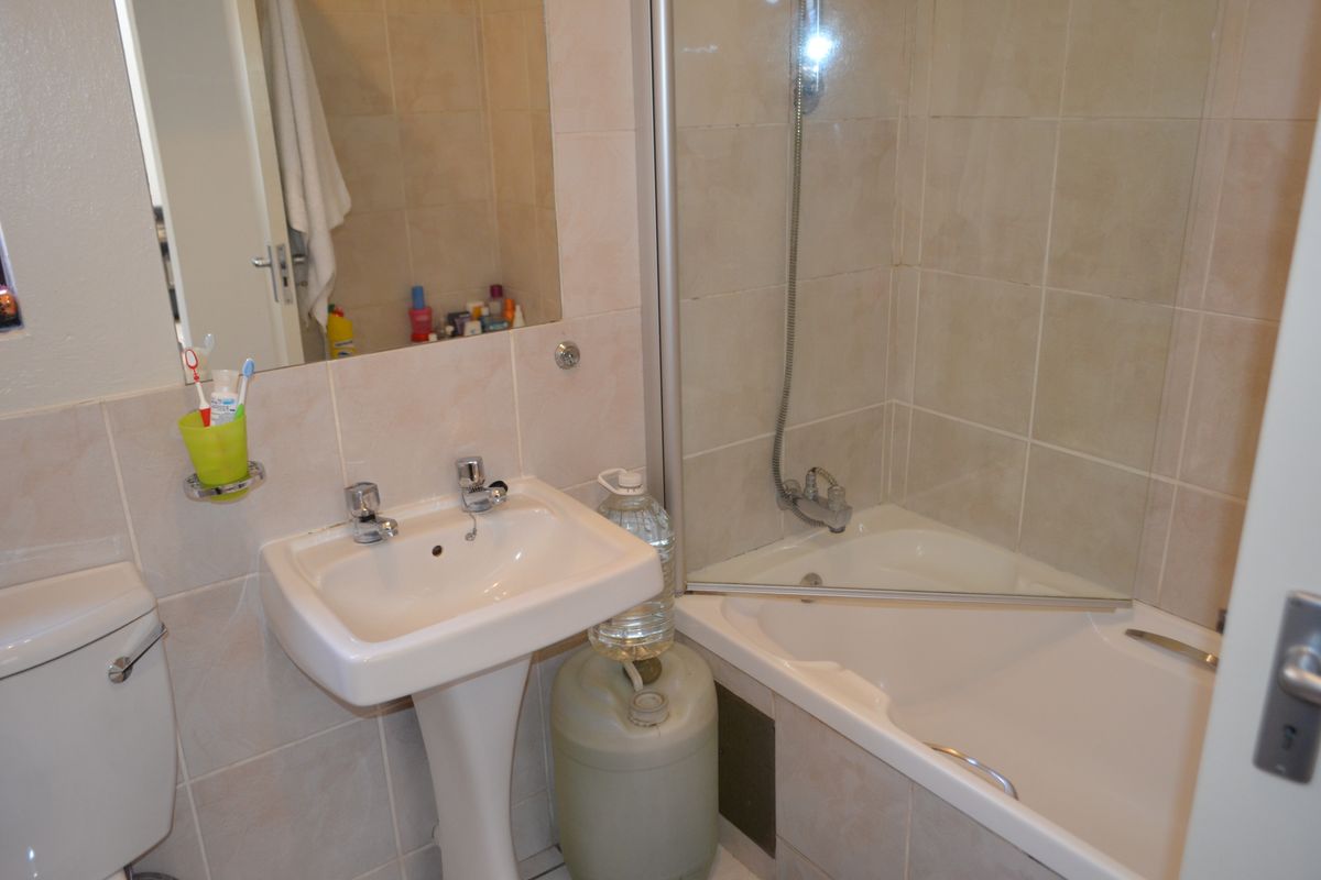 A functional bathroom featuring a pedestal basin, toilet, and a shower-over-bath combination with a glass screen and neutral wall tiling.