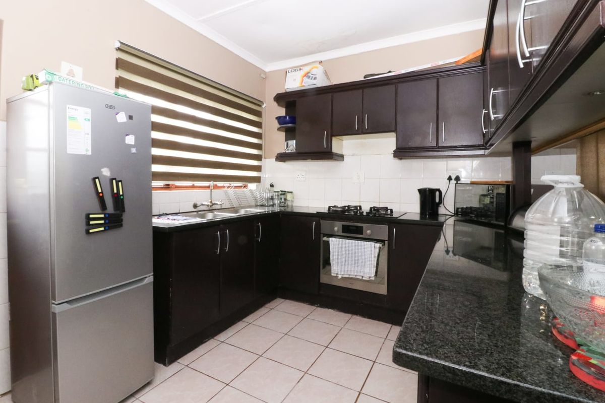 A functional kitchen featuring dark wood cabinetry, granite countertops, a built-in oven, gas hob, and tiled flooring with neutral wall finishes.