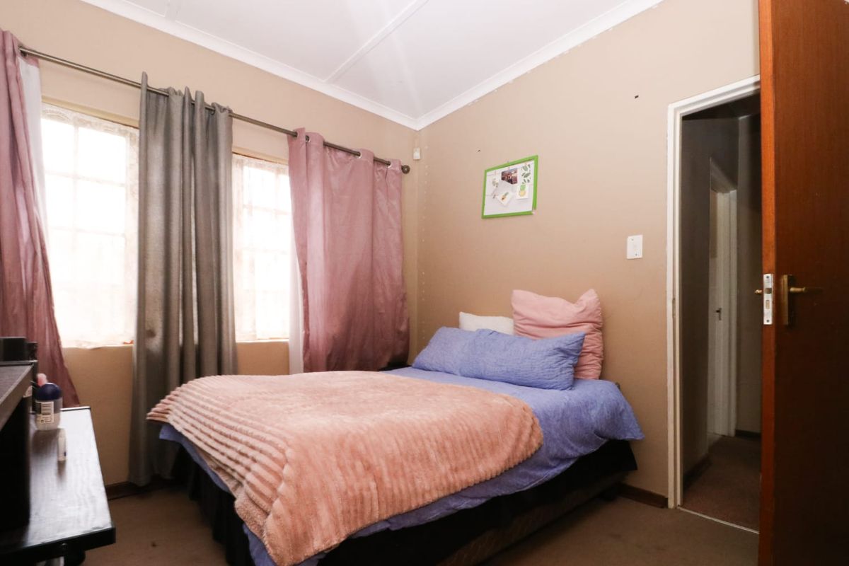 A standard bedroom featuring a window with curtain rods, a doorway leading to a hallway, and carpeted flooring.