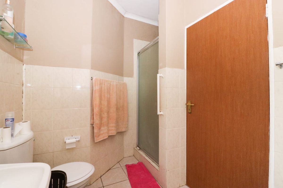 A functional bathroom featuring a shower enclosure, toilet, and washbasin with neutral wall tiling and floor tiles.