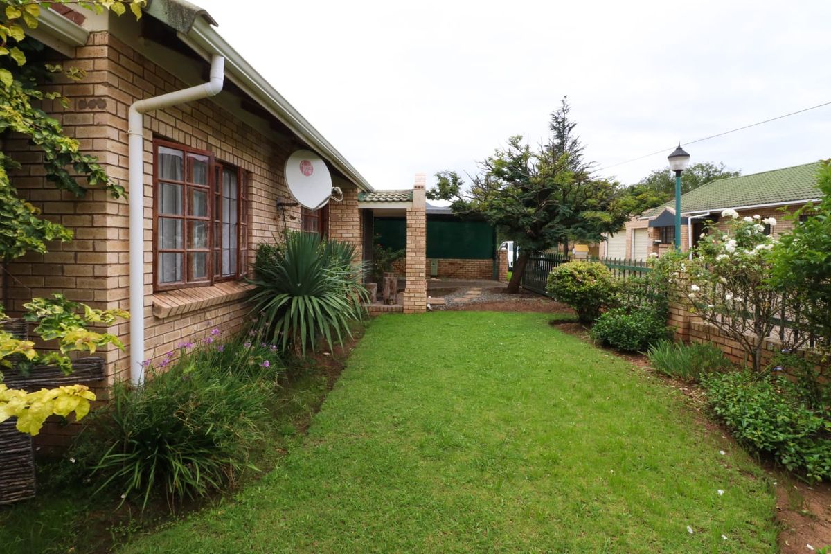 A rear exterior view of a brick townhouse featuring a small lawn, garden area, and a covered patio space.