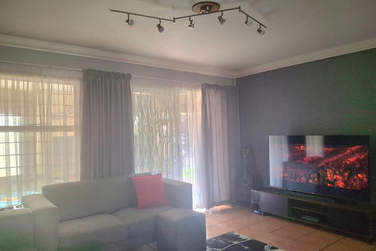 A comfortable living room featuring tiled flooring, track lighting, and a sliding glass door with security gate providing access to the exterior.