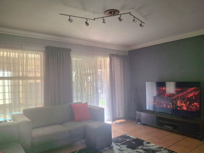 A comfortable living room featuring tiled flooring, track lighting, and a sliding glass door with security gate providing access to the exterior.