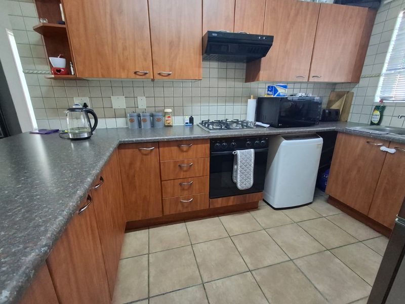 A functional kitchen featuring wood-look laminate cabinetry, gas hob, built-in oven, extractor fan, and tiled finishes throughout.