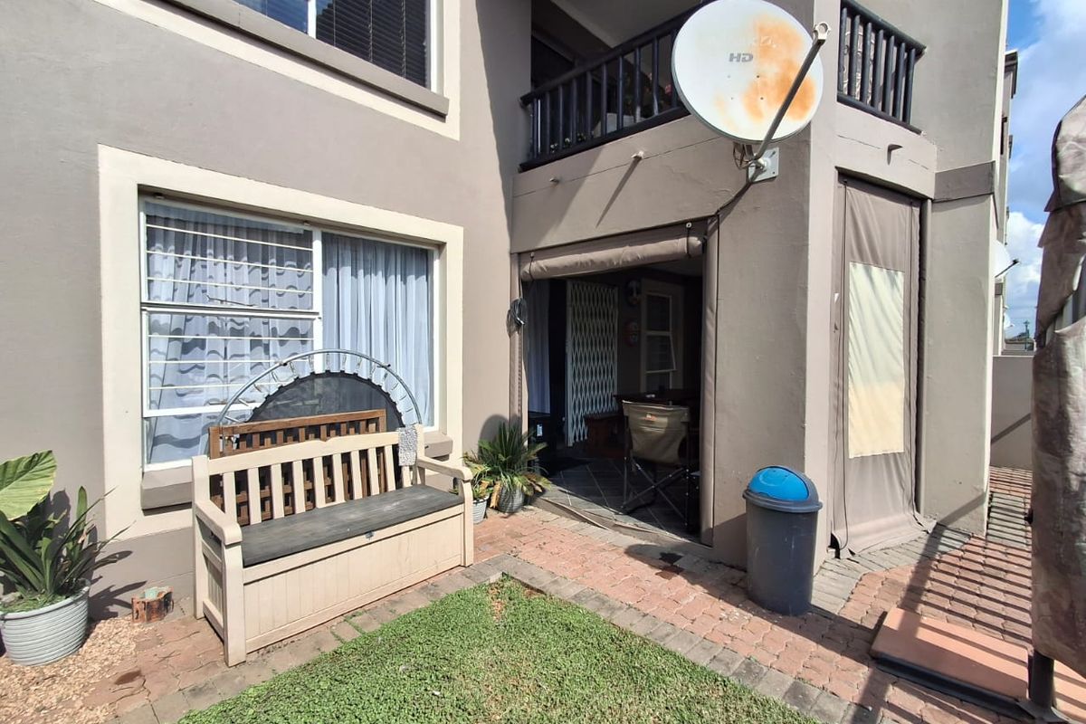 Rear exterior view of the apartment featuring a paved patio area, a small balcony above, and retractable outdoor blinds.
