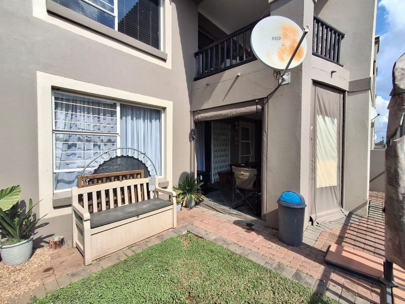 Rear exterior view of the apartment featuring a paved patio area, a small balcony above, and retractable outdoor blinds.