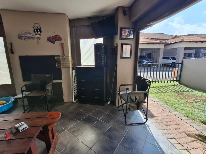 A covered patio area featuring tiled flooring and direct access to the garden and driveway, providing a functional outdoor living space.