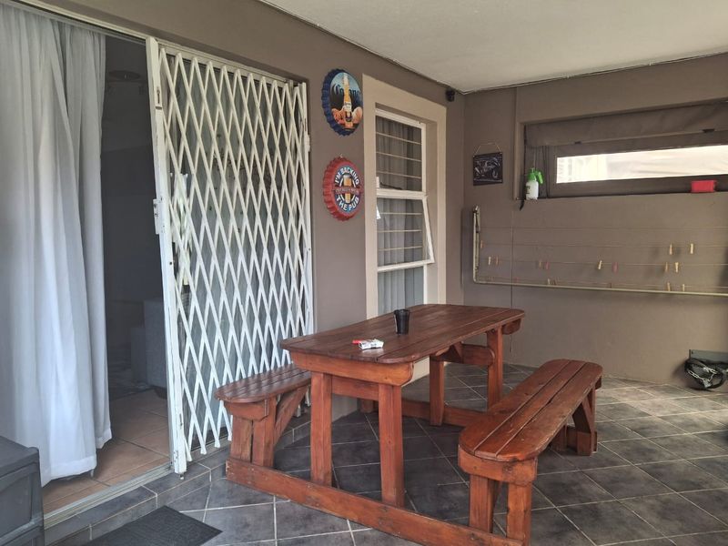 A covered patio area featuring tiled flooring, a security gate, and a wall-mounted drying rack, providing a functional outdoor space for relaxation.