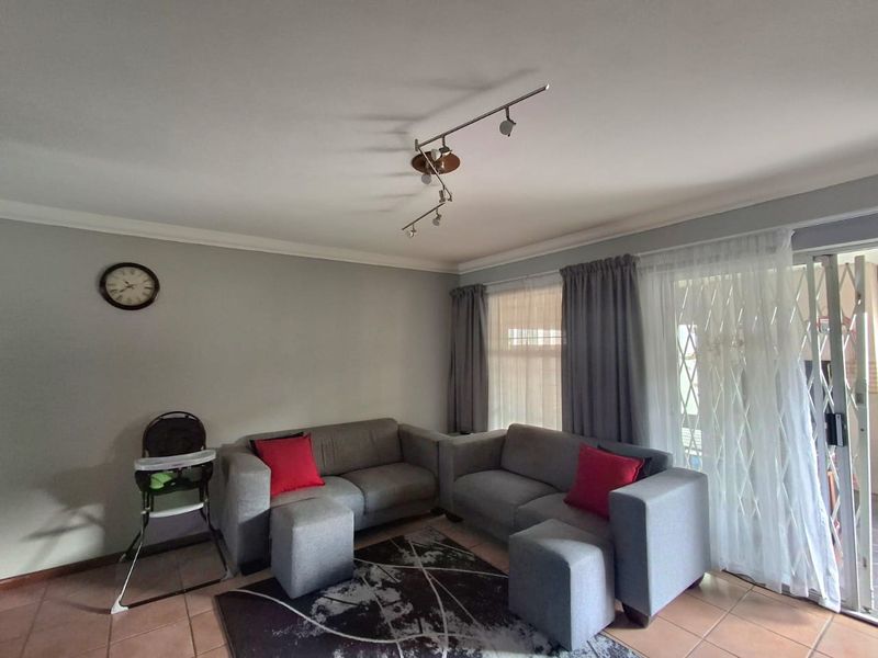 A comfortable living room featuring tiled flooring, track lighting, and a sliding glass door with a security gate leading to the exterior.