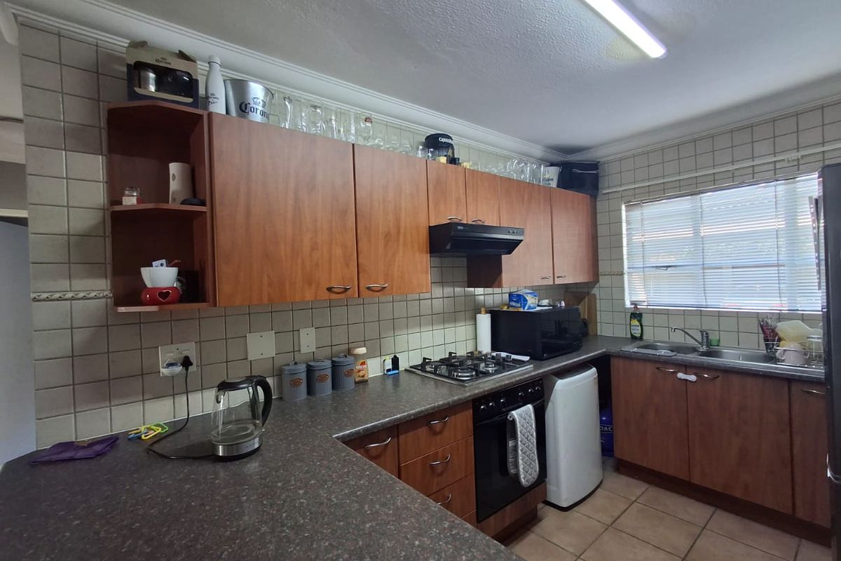 A functional kitchen featuring wood-look cabinetry, laminate countertops, a gas hob with extractor, and tiled finishes throughout.