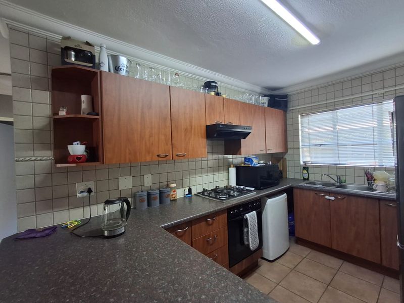 A functional kitchen featuring wood-look cabinetry, laminate countertops, a gas hob with extractor, and tiled finishes throughout.