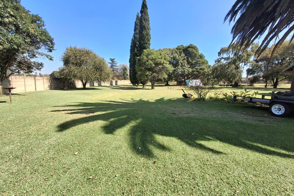 A spacious, well-maintained residential garden featuring a large lawn, mature trees, and a perimeter wall, offering ample outdoor space.