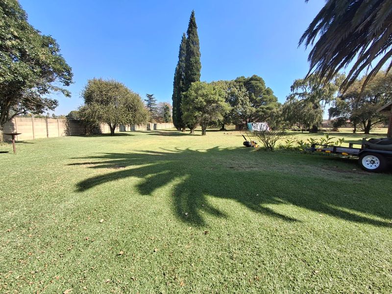 A spacious, well-maintained residential garden featuring a large lawn, mature trees, and a perimeter wall, offering ample outdoor space.