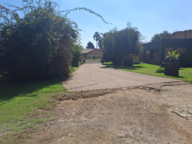 A view of the property entrance featuring a paved driveway leading to a gated access point, surrounded by established trees and lawn.