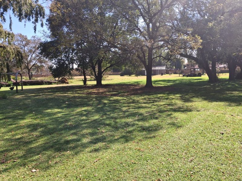 A spacious, well-maintained residential garden featuring mature trees and expansive lawn areas, offering a peaceful outdoor setting.