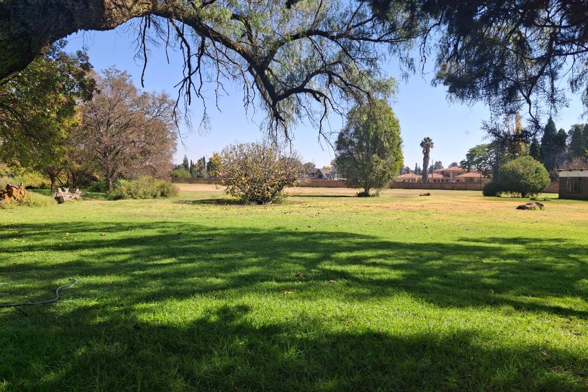 A spacious, well-maintained residential garden featuring mature trees, expansive lawn, and a perimeter wall, offering a peaceful outdoor setting.
