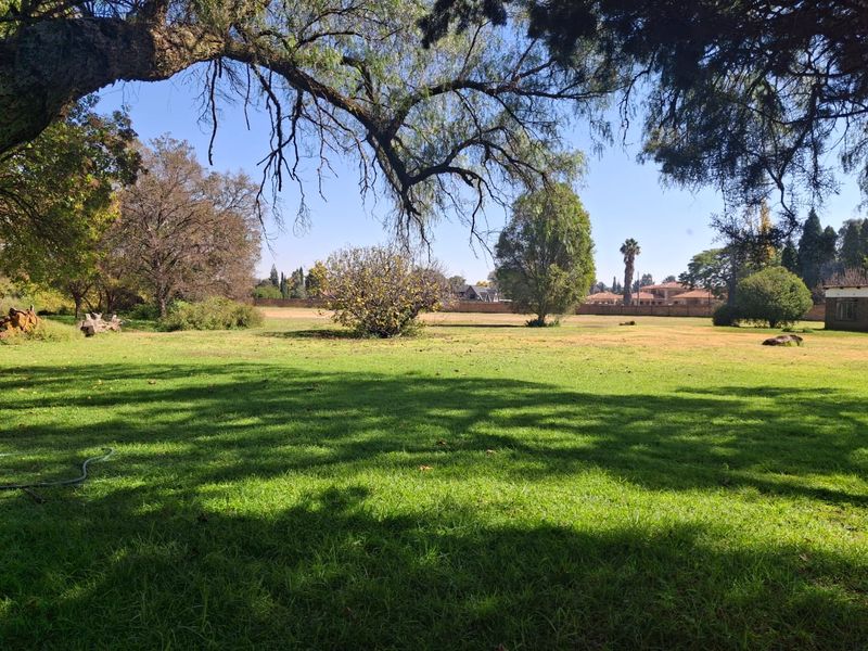 A spacious, well-maintained residential garden featuring mature trees, expansive lawn, and a perimeter wall, offering a peaceful outdoor setting.