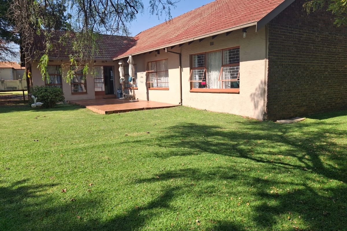 Rear view of the residential property featuring a tiled patio area, brick and plaster facade, and a well-maintained lawn.
