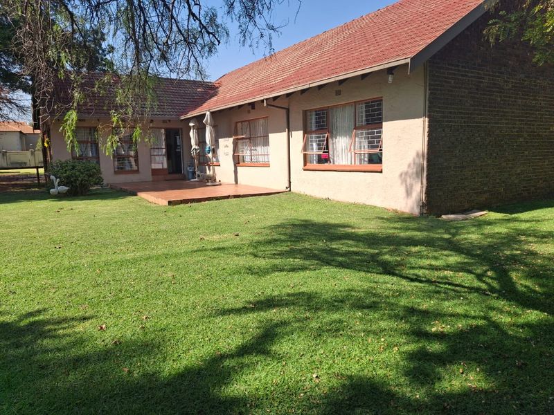 Rear view of the residential property featuring a tiled patio area, brick and plaster facade, and a well-maintained lawn.