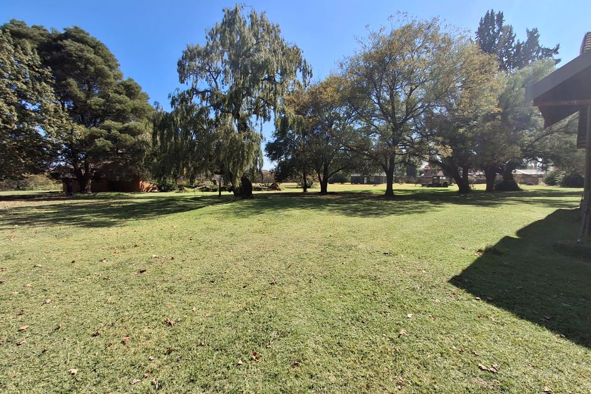 A spacious, well-maintained residential garden featuring expansive lawn areas and mature trees, offering a peaceful outdoor setting.