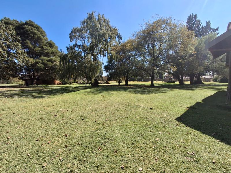 A spacious, well-maintained residential garden featuring expansive lawn areas and mature trees, offering a peaceful outdoor setting.