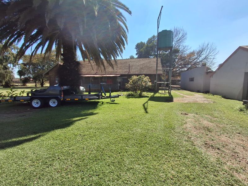 A spacious residential garden area featuring a large palm tree, a water tank on a metal stand, and views of the main dwelling.