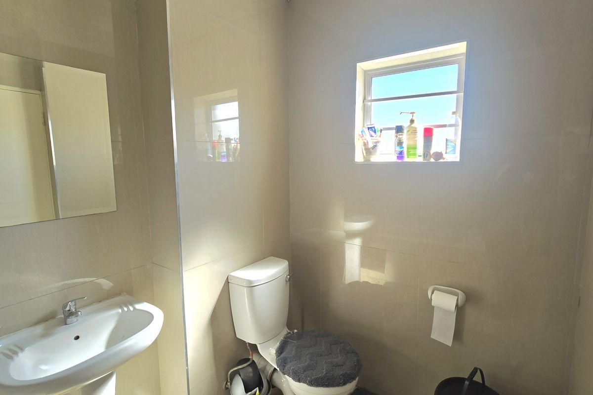 A functional bathroom featuring neutral ceramic wall tiles, a pedestal basin, a toilet, and a window providing natural light.
