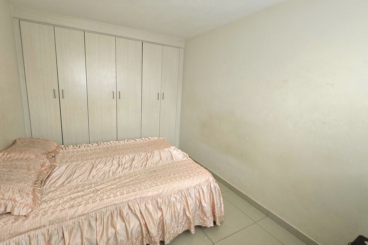 A bedroom featuring built-in cupboards and tiled flooring, requiring minor cosmetic updates to the wall finishes.