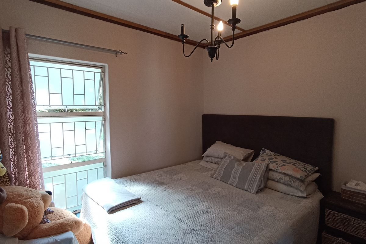 A bedroom featuring a window with security bars, a central light fixture, and timber ceiling trim.
